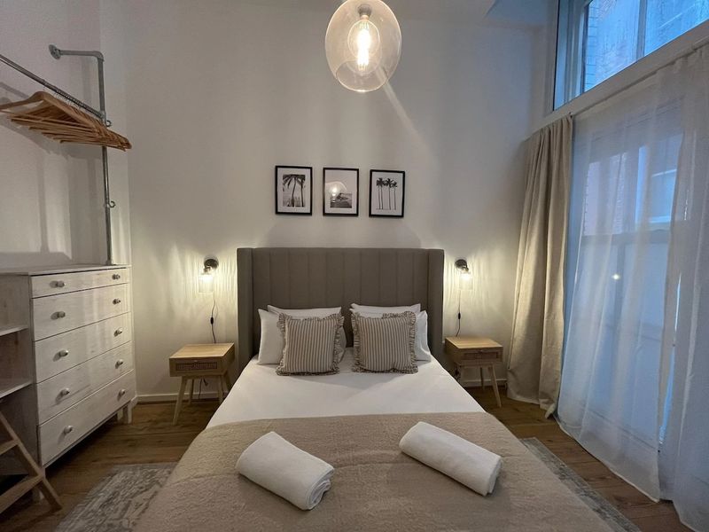 A large, king size bed situated within a warmly lit Airbnb short term rental block.